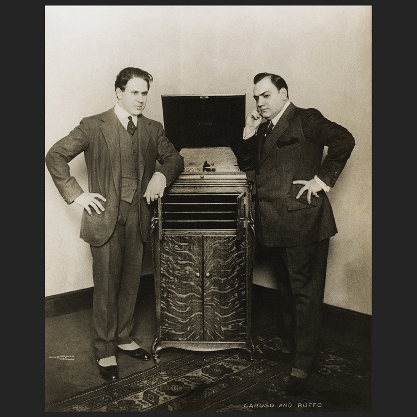 Titta Ruffo and E. Caruso (right) leaning on a Victrola phonograph, New York (date not verified)